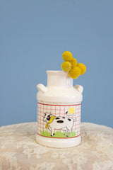 Vintage ceramic milk jug vase with a charming illustration of a cow on a red grid background.