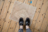 A person standing on a small vintage distressed Oushak mat in neutral beige tones.