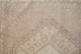 The low, even pile of a distressed Oushak mat showing geometric details in soft brown and beige.
