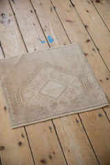 Angled view of a small, distressed Oushak rug mat with even wear and a muted neutral palette.