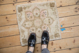 Distressed Oushak square rug with faded rose and ivory medallion, shown with feet for scale.