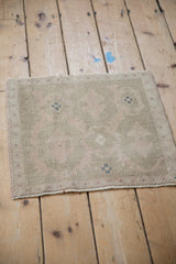 Angled view of a small vintage Oushak mat, highlighting its even wear and muted sage green palette.