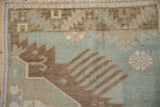 Asymmetric shrimp-like finned floral detail on distressed Oushak rug in sea foam green, bronze.