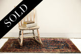 Detail of the worn royal blue Sarouk rug's shabby texture and rosy red border.