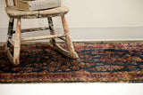 Worn Sarouk rug showcasing deep blue field, rosy red border, and tattered pile texture.
