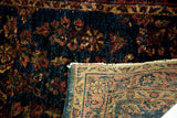 Deep blue Sarouk rug's worn pile, rosy red florals, and folded corner revealing traditional reverse.