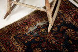 Worn texture of a vintage Sarouk rug, with deep blue field, exposed foundation, and rosy red border.