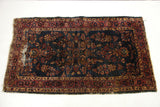Worn blue Sarouk rug's lower left corner, showing red border and visible foundation.