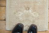 Distressed Oushak square mat in muted sand and cream tones, shown underfoot for scale.