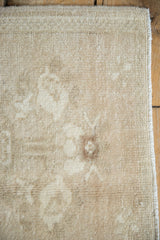 Corner of a distressed Oushak rug with low pile, faded floral motif, and intact selvage.