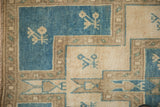Distressed Oushak rug detail: geometric tiered plant motifs with inverted dusty blue and ivory.