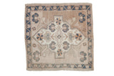 Distressed Oushak square rug with a shield medallion and floral details in beige, dusty blue, and cream.