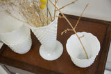 Vintage white hobnail milk glass vases showing varied textured patterns and scalloped edges.