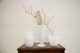 Arrangement of four vintage hobnail milk glass vases on a dark wood surface.