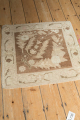 Angled view of a distressed vintage Oushak rug, highlighting its square shape and scrolled leaf pattern.