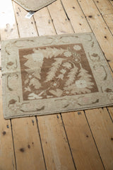 An overhead perspective on a distressed Oushak mat, showing brown scrolled leaves on ivory.