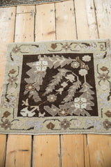 A vintage Turkish Oushak mat from an angle, highlighting its distressed texture and leaf design.