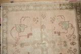 Distressed Oushak corner: dusty rose field, geometric motifs, bronze border, soft textured wear.