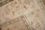Corner of distressed Oushak rug showing dusty rose pile, antique ivory foundation, and brown selvage.