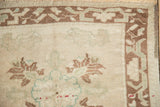 Corner detail of a distressed Oushak rug with a brown arabesque border and visible knot heads.