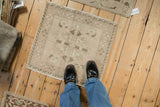 Distressed Turkish Oushak square mat, featuring faded floral medallion and wave border.