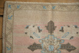 Distressed vintage Oushak rug corner, worn pile with ivory, dusty rose, and sky blue patterns.