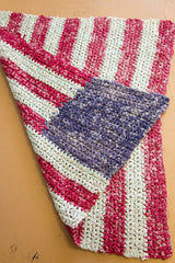 Textured corner of vintage American flag rag rug, showing red, off-white, and blue looping.