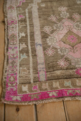 Corner of distressed vintage Oushak rug showing bright magenta border and worn pile.
