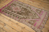 Distressed vintage Oushak rug's top corner, featuring stepped magenta patterns on coffee brown.