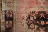 Distressed Oushak rug detail: worn pale rose, dark brown palmette motifs, serrated contour.