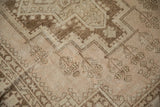 Oushak rug close-up: distressed beige and brown geometric patterns with subtle seed blossoms.
