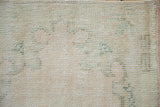Distressed Oushak rug pile showing cream, rose, and sea foam green worn texture.