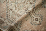 Distressed Oushak rug's folded texture, revealing worn pile, muted geometric patterns in beige and mauve.