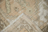 Vintage distressed Oushak rug with beige, seafoam green patterns, revealing woven foundation and fringe.