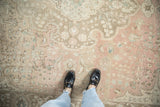 Distressed Tabriz carpet detail: dusty rose, beige, silver floral motifs, worn pile, black loafers.