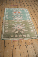 Corner of a distressed vintage Oushak rug with strong abrash, mint to olive green field, terracotta floral motifs.