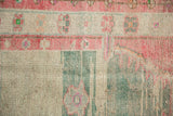 Worn pile showing knot heads and a pinwheel flower border in raspberry red and sea foam green.