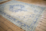 Angled view of a vintage distressed Oushak carpet, showing the worn texture and open ivory field.