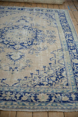 Perspective across the low-pile texture of a distressed Oushak rug with blue corner spandrels.