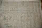 Distressed Oushak carpet's worn beige pile showing visible foundation and faint green motifs.
