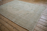Distressed Oushak carpet revealing worn texture and muted beige, faint seafoam green motifs.