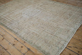 Distressed vintage Oushak carpet featuring faded cream and pale green curvilinear motifs.