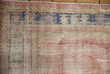 Close-up of distressed Oushak rug with faded pink pile, revealing foundation and knot heads.