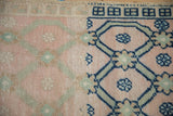 Distressed Oushak rug corner with dusty rose field, cobalt blue trellis, and square border.