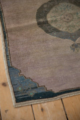 Stepped dusty dark teal spandrel and mauve abrashed field of a distressed Oushak rug.