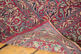 Folded vintage Persian Isfahan rug corner, revealing intricate red floral pattern and short fringe.