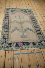 Distressed vintage Oushak rug's faded prayer design and tree of life motif seen from an angle.