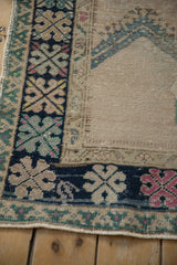 Corner of a distressed Oushak rug showing the prayer relief design and colorful geometric main border.