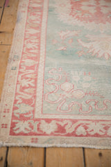 Detail of distressed Turkish Oushak rug with worn seafoam green pile, visible foundation, and faded red border.