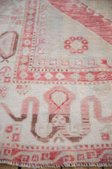 A folded corner on a distressed Oushak carpet reveals the hand-knotted reverse side.